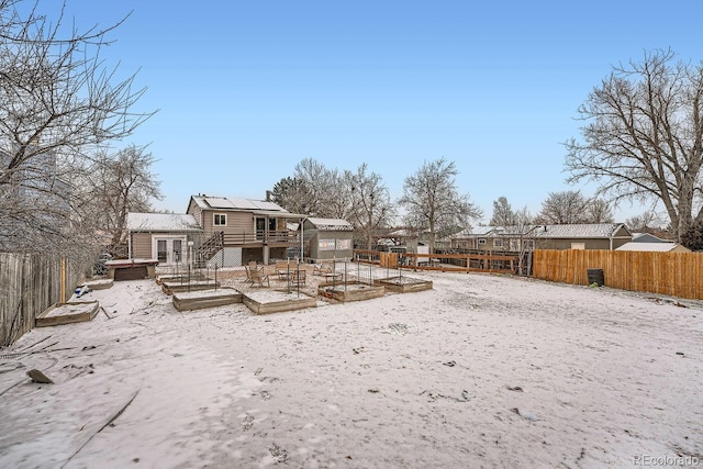 rear view of house with a vegetable garden, a fenced backyard, a greenhouse, an outbuilding, and a deck