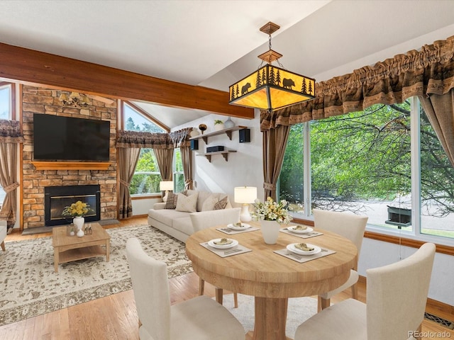 dining room with light wood-type flooring, a fireplace, vaulted ceiling with beams, and a healthy amount of sunlight