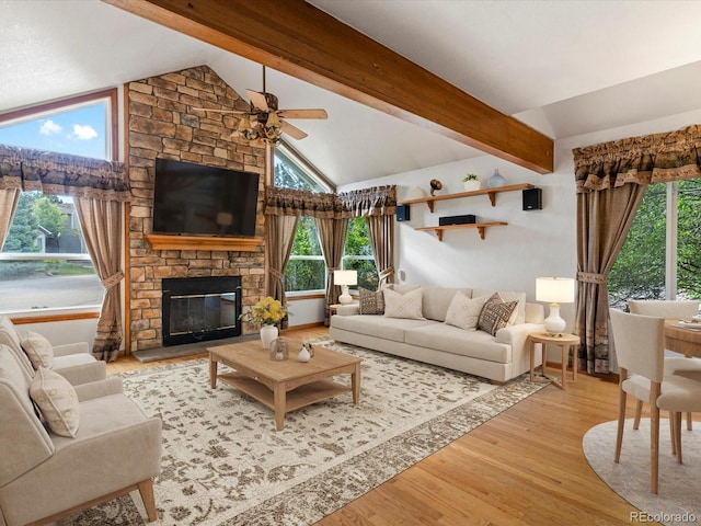 living room featuring light hardwood / wood-style flooring, a healthy amount of sunlight, a stone fireplace, and vaulted ceiling with beams