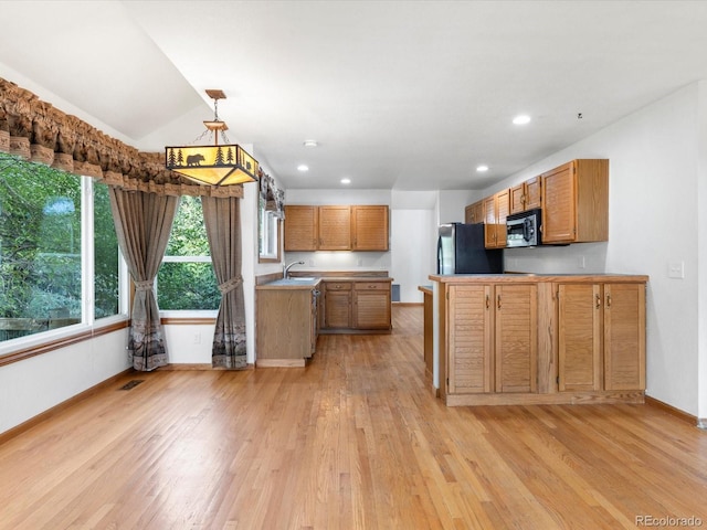 kitchen featuring light wood-type flooring, stainless steel refrigerator, decorative light fixtures, kitchen peninsula, and vaulted ceiling