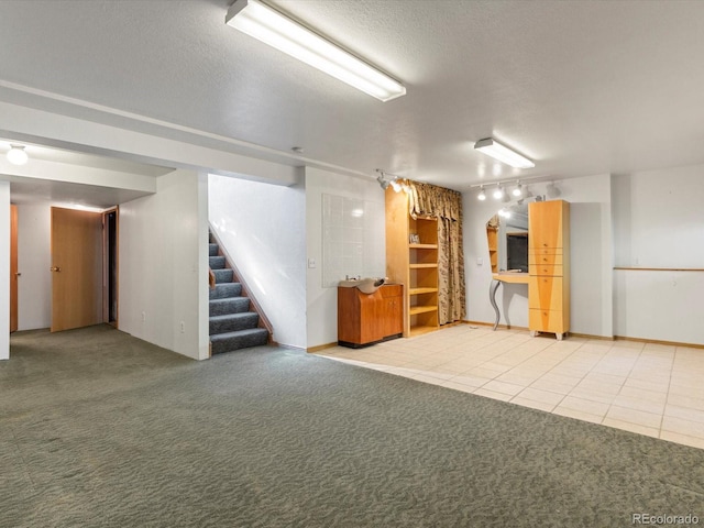 basement with rail lighting, light carpet, and a textured ceiling