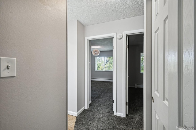 hallway featuring dark carpet, a baseboard heating unit, and a textured ceiling