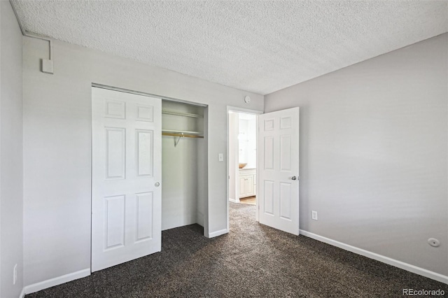 unfurnished bedroom with a closet, dark colored carpet, a textured ceiling, and baseboards