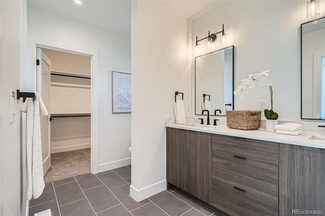 full bath featuring double vanity, a walk in closet, a sink, tile patterned floors, and baseboards