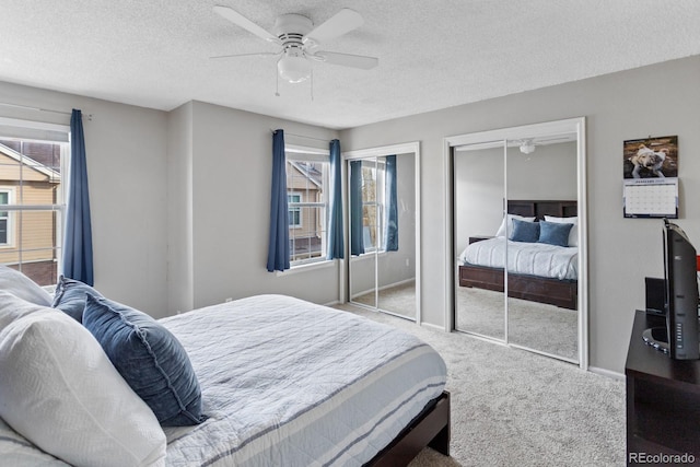 carpeted bedroom featuring a textured ceiling, two closets, and ceiling fan