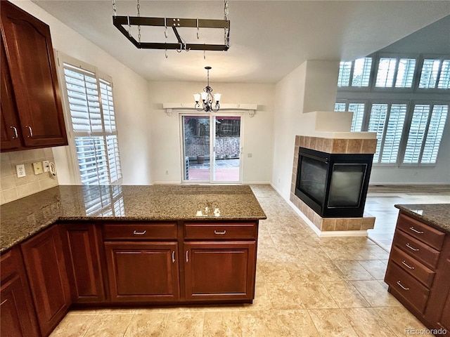 kitchen featuring pendant lighting, a healthy amount of sunlight, a fireplace, and dark stone countertops