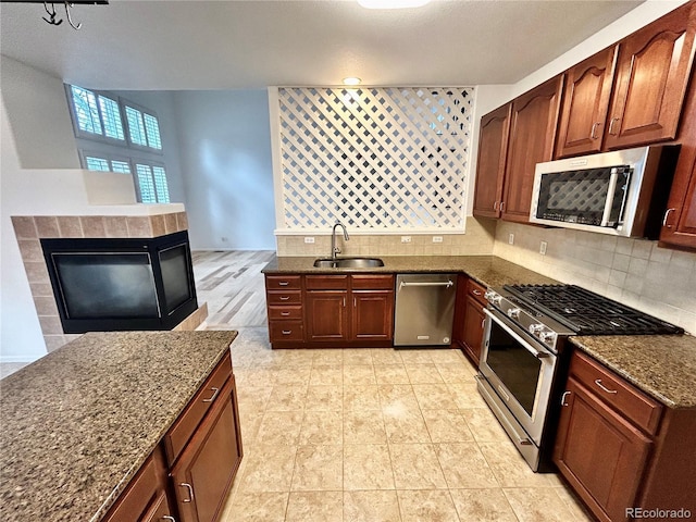 kitchen with sink, dark stone counters, stainless steel appliances, a tiled fireplace, and backsplash