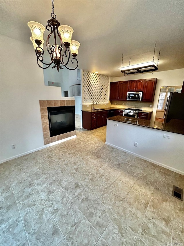 kitchen featuring sink, a tile fireplace, appliances with stainless steel finishes, backsplash, and decorative light fixtures