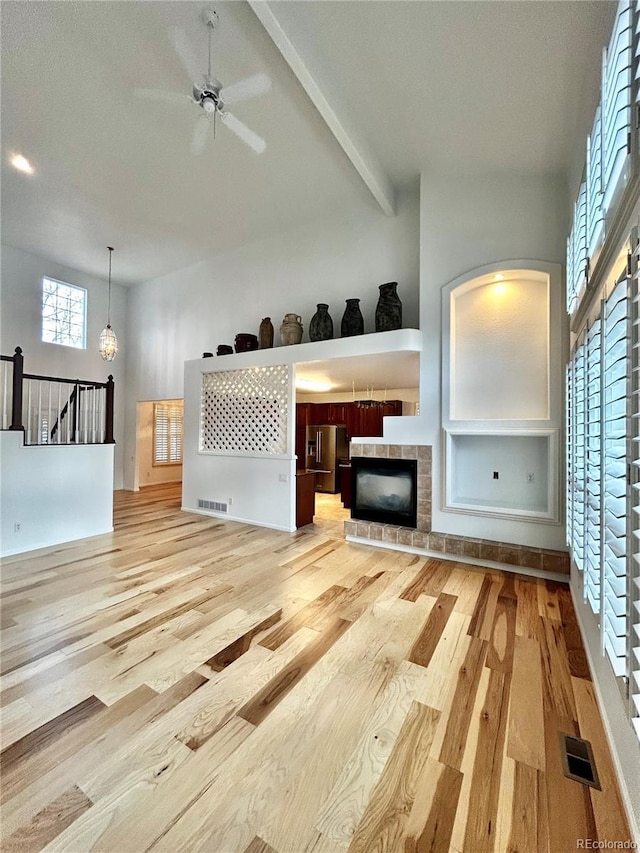 unfurnished living room with beamed ceiling, a tiled fireplace, a towering ceiling, and light hardwood / wood-style flooring