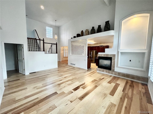 unfurnished living room featuring a high ceiling, a tile fireplace, and light hardwood / wood-style floors