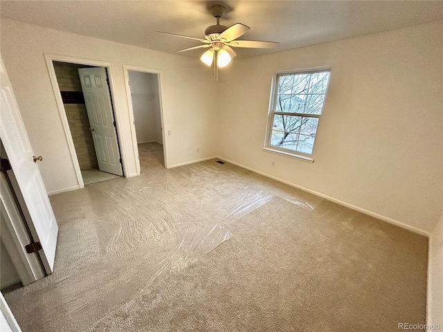 unfurnished bedroom featuring light carpet, a walk in closet, a closet, and ceiling fan