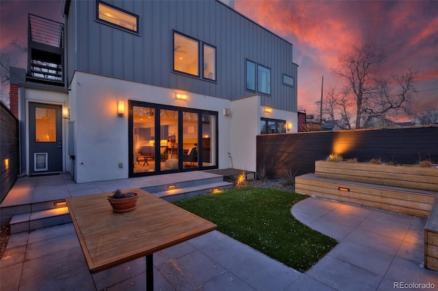 rear view of house with board and batten siding, a patio area, and fence