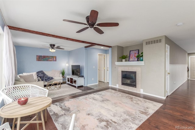 living area featuring baseboards, visible vents, dark wood finished floors, a tiled fireplace, and ceiling fan