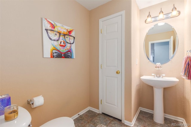 half bath with toilet, baseboards, and a sink