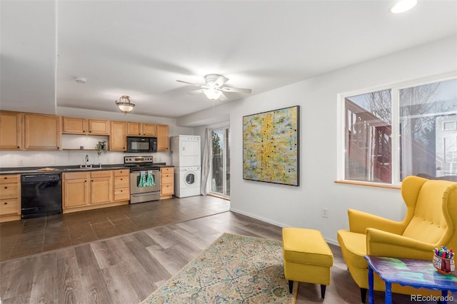 kitchen with stacked washer and clothes dryer, dark countertops, black appliances, light brown cabinets, and a sink