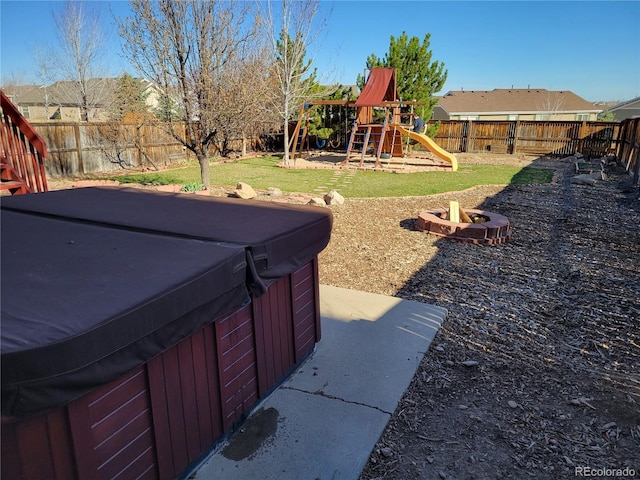 view of yard featuring an outdoor fire pit, a hot tub, a playground, and a fenced backyard