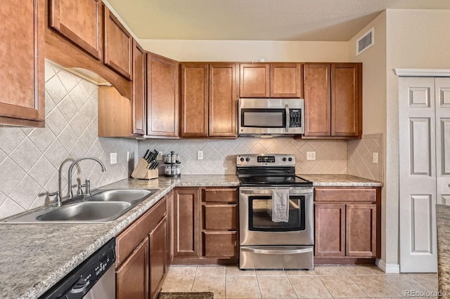 7292 S Blackhawk St Unit 2-204, Englewood, CO 80112 - kitchen featuring appliances with stainless steel finishes, a sink, brown cabinets, light tile patterned flooring, and backsplash