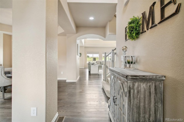 hallway featuring arched walkways, wood finished floors, a textured wall, baseboards, and recessed lighting