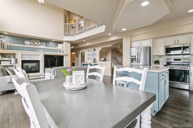 dining space featuring dark wood finished floors, recessed lighting, arched walkways, a glass covered fireplace, and stairway