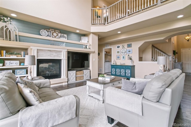 living area with wood finished floors, arched walkways, a towering ceiling, a fireplace, and recessed lighting