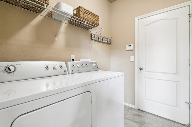 clothes washing area with washer and dryer, light marble finish flooring, and baseboards
