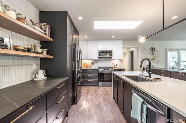 995 Chase St, Lakewood, CO 80214 - kitchen with stainless steel appliances, a skylight, light wood-style flooring, open shelves, and tasteful backsplash