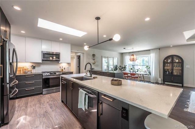 995 Chase St, Lakewood, CO 80214 - kitchen featuring appliances with stainless steel finishes, a skylight, white cabinetry, light wood-style floors, and a center island with sink