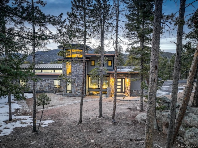 back of property at dusk with stone siding, a mountain view, a standing seam roof, and metal roof