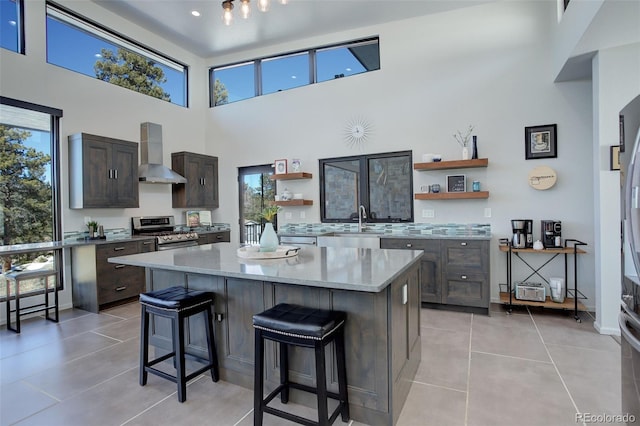 kitchen with open shelves, wall chimney exhaust hood, stainless steel gas range, and a center island