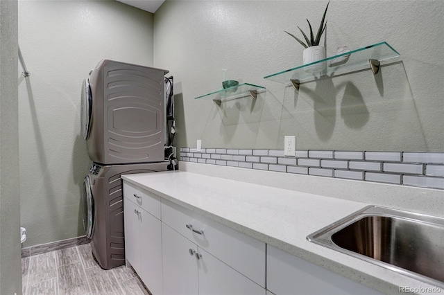 washroom with a textured wall, stacked washer / dryer, cabinet space, and wood tiled floor