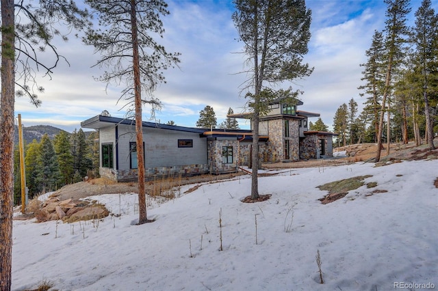 snow covered back of property with stone siding