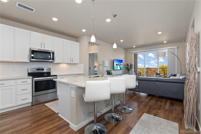 kitchen featuring stainless steel appliances, a sink, open floor plan, dark wood-style floors, and tasteful backsplash