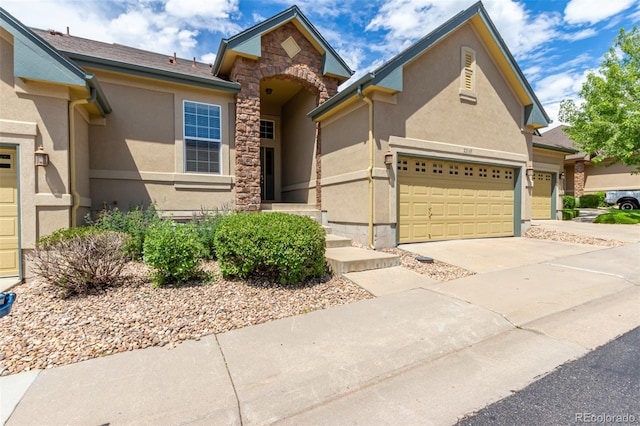 traditional-style house with a garage, stone siding, driveway, and stucco siding