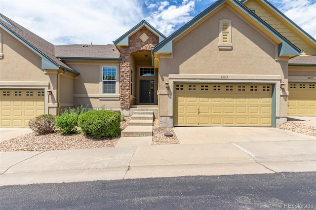 view of front of house featuring stone siding, driveway, an attached garage, and stucco siding