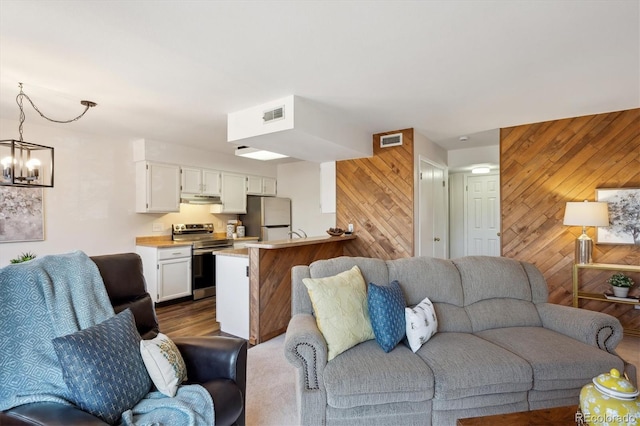 living room featuring dark wood-type flooring, visible vents, wood walls, and an inviting chandelier