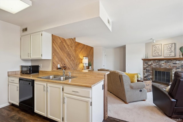 kitchen with a peninsula, a sink, open floor plan, a brick fireplace, and black appliances