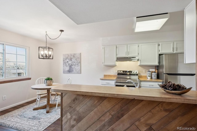 kitchen featuring baseboards, appliances with stainless steel finishes, light countertops, under cabinet range hood, and pendant lighting