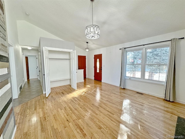 unfurnished living room with a textured ceiling, a large fireplace, high vaulted ceiling, light hardwood / wood-style flooring, and a notable chandelier