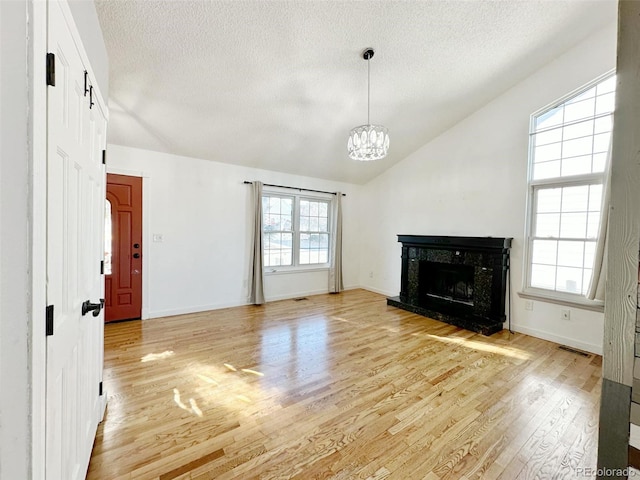 unfurnished living room with a textured ceiling, vaulted ceiling, light hardwood / wood-style flooring, a notable chandelier, and a premium fireplace