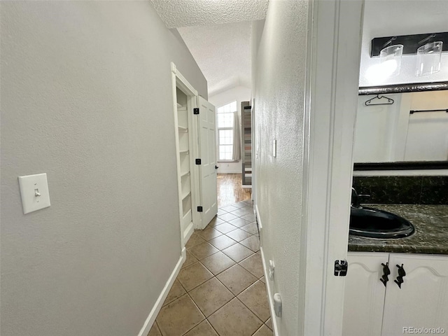 corridor featuring sink, a textured ceiling, vaulted ceiling, and light tile patterned flooring