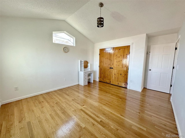 unfurnished bedroom with a textured ceiling, light hardwood / wood-style flooring, and lofted ceiling