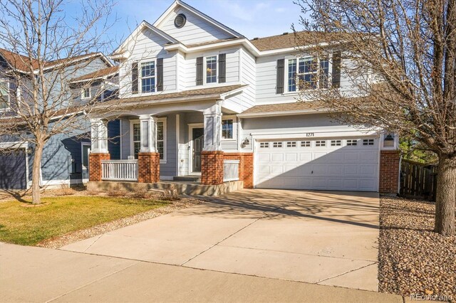 view of front of house with brick siding, covered porch, driveway, an attached garage, and a front yard