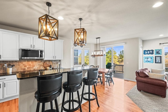 kitchen with stainless steel microwave, a chandelier, recessed lighting, backsplash, and white cabinetry