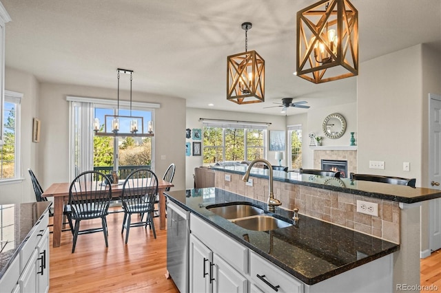 kitchen featuring a sink, dishwasher, a center island with sink, light wood-style flooring, and plenty of natural light