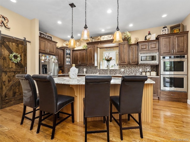 kitchen with a center island, a barn door, decorative backsplash, light wood-style floors, and stainless steel appliances