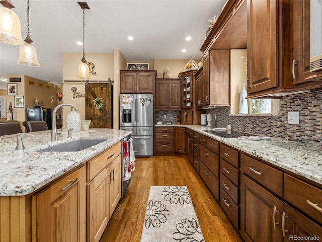 kitchen featuring light wood-style flooring, a sink, a barn door, decorative light fixtures, and stainless steel fridge