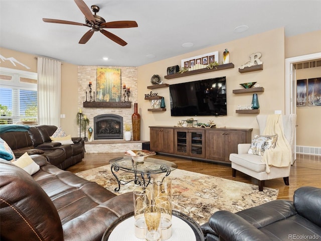 living room with a stone fireplace, wood finished floors, visible vents, and a ceiling fan