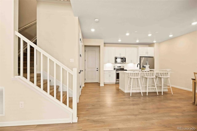 kitchen featuring stainless steel appliances, light wood-type flooring, a center island with sink, white cabinetry, and a kitchen bar