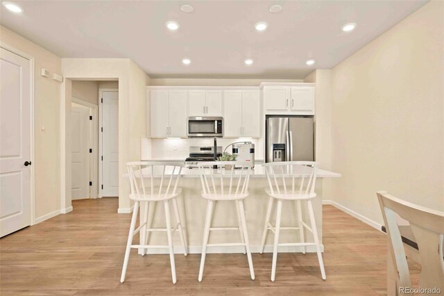 kitchen featuring a kitchen island with sink, white cabinetry, stainless steel appliances, and a kitchen bar