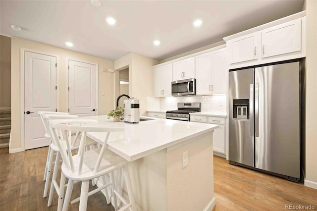 kitchen with white cabinets, a center island with sink, appliances with stainless steel finishes, and a kitchen bar